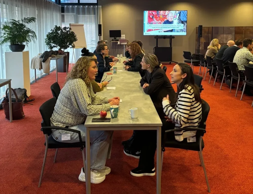 Mensen zitten tegenover elkaar aan tafels tijdens een speeddate-bijeenkomst van Werkcentrum Helmond-De Peel.