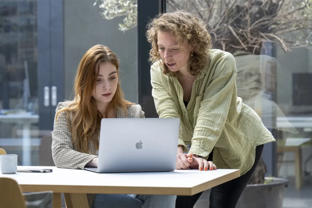 Twee collega’s werken samen achter een laptop aan een bureau.