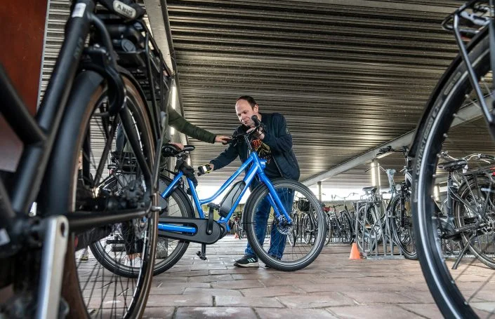 Adri controleert een blauwe fiets in de fietsenstalling.