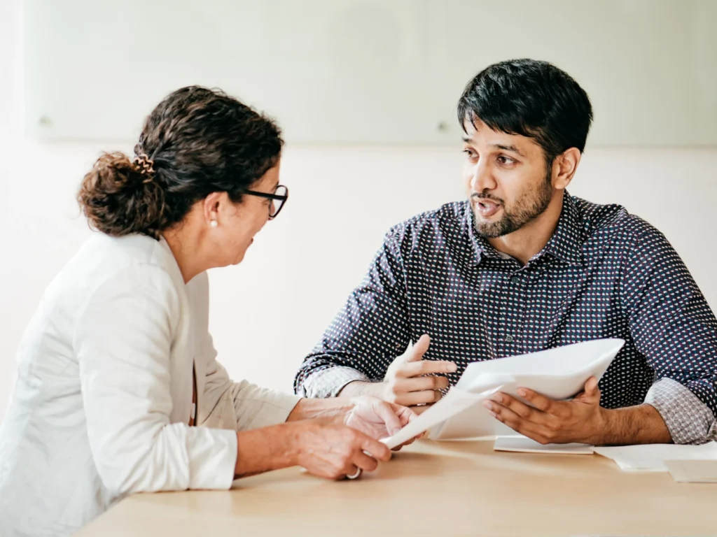 Twee personen bespreken documenten aan tafel.