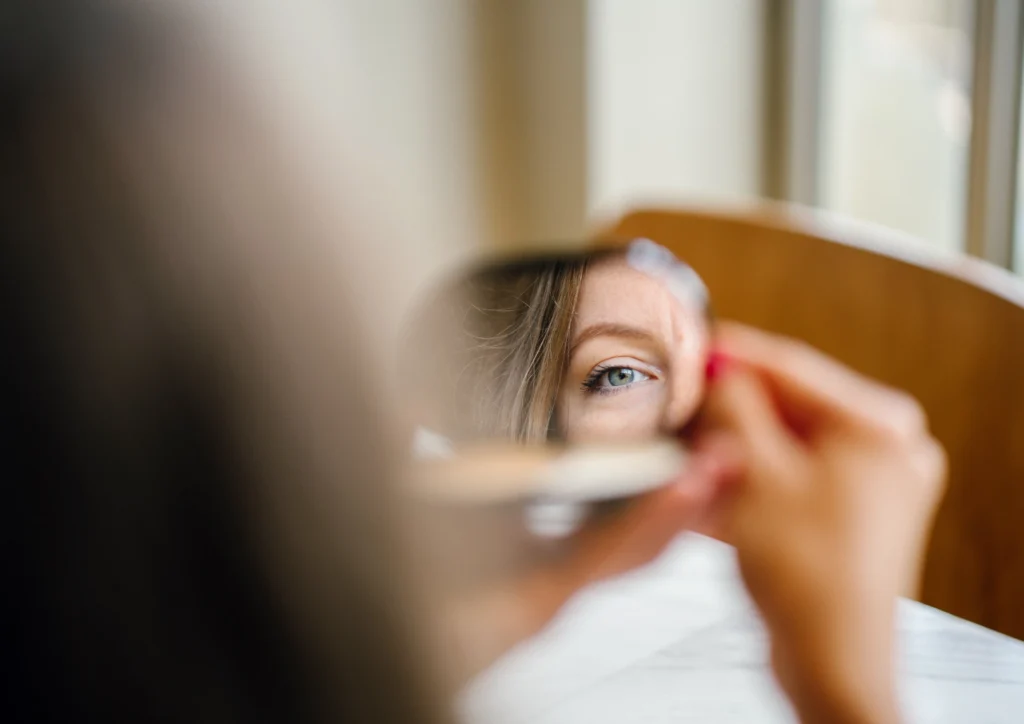 Vrouw kijkt in een kleine spiegel als metafoor voor reflectie en het vinden van nieuwe paden op de arbeidsmarkt