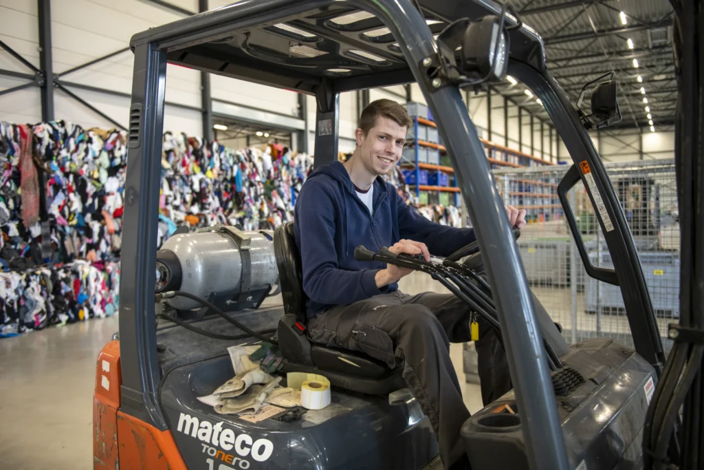 Magazijnmedewerker rijdt op een heftruck tussen stapels goederen.