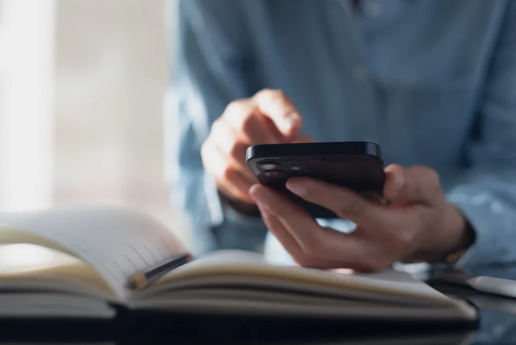 Close-up van iemand die op een smartphone kijkt en notities maakt in een open schrift.